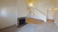 This two-floor residence offers a thoughtfully laid-out interior defined by its vaulted, angled ceilings that lend a sense of height and openness throughout. The main living area serves as a focal point, showcasing a classic stone-surround fireplace framed by tall white walls and complemented by light hardwood flooring. An open staircase rises dramatically alongside the living space, with a pendant light and upper-level window allowing natural light to filter in from above.

The kitchen is efficiently arranged with light wood cabinetry, laminate countertops, a stainless steel sink, and a full suite of appliances including a range and dishwasher, all set on easy-care hardwood-style flooring. The carpeted bedrooms feature vaulted or sloped ceilings and vertical blind-covered sliding doors or windows that invite natural light and outdoor views. Baseboard heating runs throughout, ensuring consistent warmth.

Two full bathrooms serve the residence, each equipped with a tub/shower combination. One bathroom features a wide vanity with a stone-toned countertop, a large mirror, and warm vanity lighting, while the second offers a clean, straightforward layout with wood-style flooring. The overall aesthetic is bright and neutral, providing a clean and functional canvas throughout the home.