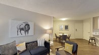 This single-floor residence offers a thoughtfully designed layout with a cohesive modern aesthetic throughout. The living room serves as the heart of the space, featuring warm hardwood-style flooring, a textured ceiling, and large vertical-blind windows that invite natural light. The room is anchored by a plush navy sofa, a sleek marble-top coffee table, and a bold black-and-white bison artwork that adds a striking focal point to the neutral palette.

Adjacent to the living area, the dedicated dining space accommodates a round white table with seating for four, accented by decorative wall art and a centrally mounted flush light fixture—ideal for both everyday meals and casual entertaining.

The kitchen is outfitted with light wood cabinetry, quartz stone countertops, a tile backsplash, a deep stainless steel sink with a modern pull-down faucet, and stainless steel appliances, offering both style and functionality.

The bedroom is a calm, restful retreat with hardwood-style flooring, a large window with exterior views, and a generous closet with open shelving and hanging storage. Warm lamp lighting enhances the serene atmosphere.

The bathroom features a vanity with quartz countertops, wood-toned cabinetry, and a shower/tub combination, completing this well-rounded and move-in ready space.