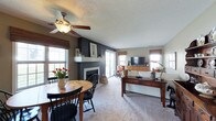 This single-floor space showcases an open-concept design that seamlessly connects the dining and living areas, creating a cohesive and functional layout. The living room serves as the focal point of the home, anchored by a sleek fireplace set against a striking dark accent wall that contrasts beautifully with the lighter neutral tones throughout the rest of the space. A white mantel provides a clean architectural detail, while the surrounding wall adds a bold, modern touch to the overall design.

Plush wall-to-wall carpeting runs throughout both the living and dining areas, adding warmth and comfort underfoot. The living room is well-appointed with comfortable seating, a wood-toned media console, and a wall-mounted flat-screen television, all positioned to take advantage of the natural light streaming in through multiple windows dressed in warm bamboo shades. A sliding glass door opens to an outdoor patio, enhancing the sense of openness and connectivity to the exterior.

The dining area features a natural wood table paired with classic black Windsor chairs, with a ceiling fan overhead providing comfort and airflow. A textured popcorn ceiling is consistent throughout, completing this inviting, well-balanced living space.