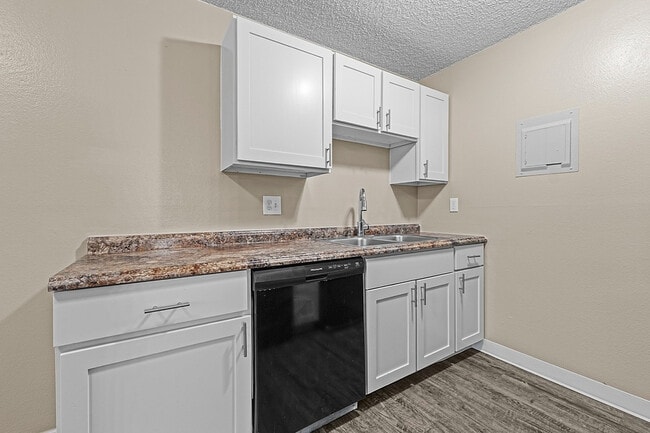 Cocina moderna con elegantes gabinetes blancos y encimeras de granito, que cuenta con un fregadero doble. - Glen Ridge Apartments