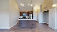 This single-floor residence in Montgomery, Illinois offers a thoughtfully designed open-concept layout highlighted by dramatic vaulted ceilings that lend a sense of grandeur throughout the main living area. The kitchen serves as a central focal point, anchored by a large island with a white quartz countertop, an integrated sink, and stylish pendant lighting overhead. Rich dark-toned cabinetry pairs with a subway tile backsplash and a full suite of stainless steel appliances, including a refrigerator, microwave, and range. Wood-look plank flooring extends seamlessly across the kitchen and living area, complementing the neutral wall tones. The expansive living space accommodates multiple furniture arrangements and is enhanced by a ceiling fan and an elegant chandelier. Natural light filters in through multiple windows fitted with horizontal blinds. The bedrooms feature plush carpeting, ceiling fans, generous windows, and well-organized walk-in closets with built-in shelving. The bathroom includes a full soaking tub with a shower surround, brushed nickel fixtures, and wood-look flooring. A dedicated entry area provides a practical transition into the living space.