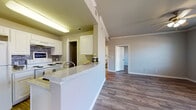 This single-story residence offers a cohesive and functional layout finished with rich, dark wood-look flooring that extends throughout the living areas, bedrooms, and bathrooms, providing a warm and consistent aesthetic. Crown molding accents the main living spaces, adding a refined architectural detail that complements the neutral gray wall tones.

The kitchen is designed for practicality and style, featuring white cabinetry with ample storage, light granite-style countertops, a tiled backsplash, and white appliances including a range and refrigerator. A peninsula with a built-in sink creates a natural divide between the kitchen and the open living area, ideal for both meal preparation and casual dining. A dedicated pantry or utility closet is accessible directly from the kitchen.

The living and bedroom spaces are generously proportioned, each benefiting from multiple windows dressed with horizontal blinds that allow for controlled natural light. Ceiling fans with integrated lighting fixtures are present in the primary rooms, enhancing comfort year-round.

The bathrooms are clean and well-finished, with one featuring a white vanity, a framed mirror, and modern light fixtures, while another includes a full soaking tub with white tile surround. The overall ambiance of the space is bright, neutral, and move-in ready.