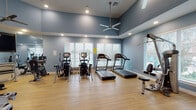 Located at 2250 Sara Jane Pkwy in Grand Prairie, Texas, this single-floor fitness center is thoughtfully designed to support a comprehensive workout experience. The space is finished with warm light hardwood flooring throughout and features calming blue-toned walls that lend a clean, modern aesthetic. Elevated tray ceilings add a sense of spaciousness, while multiple ceiling fans and recessed lighting ensure the environment remains comfortable and well-lit during any workout.

Natural light pours in through several large windows fitted with white horizontal blinds, offering views of the surrounding outdoor area. A full-length mirror along one wall visually expands the space and supports form monitoring during exercise.

The cardio zone is well-equipped with multiple treadmills, elliptical trainers, and stationary bikes, all arranged to maximize usable floor space. The strength training area features a multi-station cable machine, weight benches, and a selection of additional resistance equipment, providing options for both beginners and experienced athletes. A wall-mounted flat-screen television adds entertainment value to the space.

A sanitizing station and clearly marked exit signage reflect attention to health and safety standards. An adjoining room, visible through glass-paneled doors, further extends the facility's functionality. Overall, this fitness center delivers a well-rounded, accessible, and inviting environment for daily exercise.
