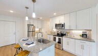 Located at 16100 Myriad Lane in Fort Myers, FL, this 2-bedroom, 2-bathroom unit offers a thoughtfully designed single-floor layout. The open-concept kitchen, dining, and living area serves as the heart of the home, highlighted by a large granite-topped island with a built-in sink, crisp white shaker cabinetry, a subway tile backsplash, and a full suite of stainless steel appliances. Pendant lighting and recessed fixtures provide warm, layered illumination throughout. Light wood-style flooring runs seamlessly across the main living areas and bedrooms, enhancing the bright, airy atmosphere. Sliding glass doors in the living area open to a private patio, allowing natural light to flow into the space. The spacious primary bedroom connects to one of two well-appointed bathrooms, each featuring granite vanity countertops, white cabinetry, and a tub-shower combination. The second bedroom offers a clean, versatile space suitable for various uses. Additional conveniences include three closets, a dedicated pantry, and an in-unit laundry area with a stacked washer and dryer. The overall aesthetic is modern and cohesive, with a neutral palette that creates a welcoming, move-in-ready environment.