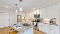 Located at 16100 Myriad Lane in Fort Myers, FL, this 2-bedroom, 2-bathroom unit offers a thoughtfully designed single-floor layout. The open-concept kitchen, dining, and living area serves as the heart of the home, highlighted by a large granite-topped island with a built-in sink, crisp white shaker cabinetry, a subway tile backsplash, and a full suite of stainless steel appliances. Pendant lighting and recessed fixtures provide warm, layered illumination throughout. Light wood-style flooring runs seamlessly across the main living areas and bedrooms, enhancing the bright, airy atmosphere. Sliding glass doors in the living area open to a private patio, allowing natural light to flow into the space. The spacious primary bedroom connects to one of two well-appointed bathrooms, each featuring granite vanity countertops, white cabinetry, and a tub-shower combination. The second bedroom offers a clean, versatile space suitable for various uses. Additional conveniences include three closets, a dedicated pantry, and an in-unit laundry area with a stacked washer and dryer. The overall aesthetic is modern and cohesive, with a neutral palette that creates a welcoming, move-in-ready environment.