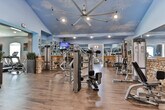 Located at 165 Reservoir Dr in Canton, Georgia, this fitness facility combines a rustic-modern aesthetic with a comprehensive range of workout equipment across a single-floor layout. The design throughout is defined by a signature blend of natural stone accent walls, warm wood trim, and rich hardwood-style flooring that creates an inviting and motivating atmosphere.

The main workout area is expansive and open, featuring a striking sky-blue ceiling mural complete with clouds and a large industrial ceiling fan that enhances airflow across the floor. Full-length mirrors line the walls, amplifying the sense of space and allowing members to monitor their form. The floor is stocked with a wide selection of strength-training machines and cable equipment, thoughtfully arranged to allow comfortable movement between stations.

A dedicated cardio room provides a more intimate workout setting, furnished with commercial-grade treadmills and rowing machines. Arched windows allow natural light to fill the space, while wall-mounted televisions keep members entertained during cardio sessions. Motivational phrases such as "Work For It" and "Do It For The After Photo" are displayed on the walls, reinforcing the facility's encouraging and goal-oriented culture.

The overall ambiance is polished yet approachable, balancing aesthetic character with functional fitness design throughout every area of the space.
