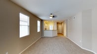 Located at 1100 Garden View in Encinitas, California, unit #325 is a single-floor residence offering a clean, functional layout with a welcoming, neutral aesthetic throughout. The open-concept living area is finished with plush wall-to-wall carpeting, providing a comfortable and quiet underfoot feel. Large windows fitted with blinds allow natural light to fill the space, enhancing the airy, bright atmosphere. A ceiling fan is centrally positioned overhead, offering both circulation and ambient lighting to the living area. The living space flows seamlessly into a kitchen featuring a peninsula-style breakfast bar, white cabinetry, and recessed lighting that creates a warm, well-lit cooking and dining environment. The kitchen's open sightlines connect it naturally to the living area, making the layout ideal for everyday living. Beyond the kitchen, a hallway leads to additional rooms, with interior doors providing privacy and separation. The unit's color palette of warm beige and soft white tones throughout the walls and ceilings creates a cohesive, move-in-ready environment. Recessed lighting in the kitchen and hallway, combined with the natural light from the living area windows, ensures the space remains bright and inviting throughout the day.
