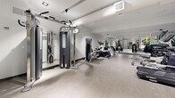 Located at 41 Dundonald Street in Toronto's Church-Wellesley Village, this fitness centre offers a thoughtfully organized workout facility across a single floor. The space features a clean, modern aesthetic with light grey stone-effect flooring, white ceilings with recessed and track lighting, and soft blue accent walls that lend a calm, motivating atmosphere throughout.

The gym is comprehensively equipped to support a full-body workout routine. Cardio options include a treadmill, elliptical trainers, and a stationary bike, all positioned with ample space between them. A dedicated strength training area features a multi-function cable machine, a weight bench, and a well-stocked dumbbell rack covering a range of weights. For functional fitness and flexibility, a storage rack holds medicine balls, stability balls, resistance bands, and foam rollers.

Full-length mirrored walls span a large section of the facility, visually expanding the space and providing users with proper form feedback during exercise. The layout is efficiently arranged to maximize usability without feeling crowded. Recessed ventilation and climate control ensure a comfortable environment. The overall design is sleek and contemporary, making this fitness centre a practical and inviting amenity.