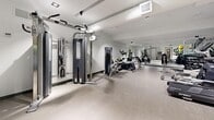 Located at 41 Dundonald Street in Toronto's Church-Wellesley Village, this fitness centre offers a thoughtfully organized workout facility across a single floor. The space features a clean, modern aesthetic with light grey stone-effect flooring, white ceilings with recessed and track lighting, and soft blue accent walls that lend a calm, motivating atmosphere throughout.

The gym is comprehensively equipped to support a full-body workout routine. Cardio options include a treadmill, elliptical trainers, and a stationary bike, all positioned with ample space between them. A dedicated strength training area features a multi-function cable machine, a weight bench, and a well-stocked dumbbell rack covering a range of weights. For functional fitness and flexibility, a storage rack holds medicine balls, stability balls, resistance bands, and foam rollers.

Full-length mirrored walls span a large section of the facility, visually expanding the space and providing users with proper form feedback during exercise. The layout is efficiently arranged to maximize usability without feeling crowded. Recessed ventilation and climate control ensure a comfortable environment. The overall design is sleek and contemporary, making this fitness centre a practical and inviting amenity.