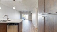 Located at 9901 Lurline Ave in the Chatsworth neighborhood of Los Angeles, this thoughtfully designed unit makes efficient use of its single-floor layout. The open-concept kitchen and living area serve as the heart of the space, seamlessly connecting day-to-day living and dining functions. The kitchen is outfitted with rich dark-wood cabinetry, a light quartz countertop peninsula with an undermount double sink, stainless steel appliances including a refrigerator, range, microwave, and dishwasher, and elegant pendant lighting overhead. Light wood-style flooring extends throughout, contributing to a cohesive, modern aesthetic. The living area is distinguished by vaulted ceilings with exposed white-painted wood beams, lending architectural character and an airy sense of height. A sliding glass door opens onto a private balcony, framing views of lush palm trees and the landscaped courtyard below. Two bathrooms round out the layout — one featuring dark-framed frosted glass sliding closet doors, wood-finish cabinetry, and a sleek vanity, while the second offers a clean, all-white tub-shower combination. A wall-mounted AC unit ensures year-round comfort. The overall ambiance is fresh, modern, and move-in ready.