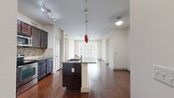 This single-floor, 2-bedroom, 2-bathroom residence offers a thoughtfully designed open-concept layout that maximizes comfort and functionality. The kitchen serves as the centerpiece, featuring dark espresso cabinetry, granite countertops, a tile mosaic backsplash, stainless steel appliances, and a central island with a built-in sink and pendant lighting — including a distinctive red accent pendant. The kitchen flows seamlessly into the living area, which is finished with rich hardwood flooring, a ceiling fan, and a large sliding glass door dressed in vertical blinds that fills the space with natural light. Both bedrooms are carpeted and offer a calm, neutral palette, with the primary bedroom providing generous proportions and access to a spacious walk-in closet with built-in shelving and hanging rods. The primary bathroom is particularly well-appointed, featuring dual granite-topped vanities with dark cabinetry, large-format tile flooring, a soaking tub, a separate glass-enclosed shower with decorative tile accents, and direct access to the walk-in closet. A second full bathroom mirrors the refined finishes found throughout. Hallways connect the spaces efficiently, while two dedicated closets provide ample storage across the residence.