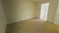 This two-floor residential space is designed with a straightforward, functional layout that emphasizes comfort and practicality. The interior is finished in soft, neutral cream tones throughout, creating a clean and cohesive aesthetic across both levels. Carpeted flooring runs through the main living areas, adding warmth underfoot, while sections of hard flooring are also present, offering a contrast in texture and material. The rooms are generously proportioned, with open wall space that allows for flexible furniture arrangements. Natural light filters in through windows, brightening the interiors and enhancing the airy feel of the space. Louvered bifold closet doors are a notable recurring feature, providing ample storage capacity in key areas. The layout includes interconnected rooms accessible through wide doorways, promoting a smooth flow between spaces. Ceiling-mounted HVAC vents are visible, ensuring climate control throughout. White trim and baseboards frame each room neatly, complementing the light wall colors. Overall, the space presents a clean, move-in ready environment with a calm, understated ambiance suited to a variety of living arrangements.