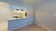 Located at 635 Anson St in Winston-Salem, NC, this single-story unit offers a straightforward, functional layout with a cohesive design throughout. The interior is finished with light-toned ceramic tile flooring across the main living and kitchen areas, complemented by clean white baseboards and crown molding that frame each room consistently.

The kitchen is positioned behind a peninsula-style counter that opens to the adjacent dining or living area, creating an efficient pass-through design. White upper cabinetry, a built-in cooktop, sink, and an under-cabinet range hood provide practical workspace, while the open counter connects the kitchen visually to the surrounding space. The dining area and living spaces are painted in a soft blue-gray tone, lending a calm, neutral atmosphere throughout.

The bedrooms feature a warmer neutral palette, with one room finished in carpet and another in tile, each equipped with windows that allow natural light to filter in. Crown molding carries through these rooms as well, maintaining a consistent architectural detail. A bathroom includes a full tub-shower combination with white tile surround. One room features an exposed painted brick wall, adding a subtle textural element. The layout flows efficiently from the front entry through the living and kitchen zones toward the private rooms at the rear.