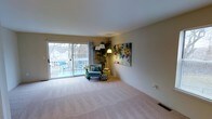 This well-appointed multi-floor residence offers a thoughtfully designed layout spread across three levels, providing ample space and functionality. The living area is a standout feature, bathed in natural light streaming through large sliding glass doors that open onto an outdoor deck or balcony. The deck extends the living space outdoors, offering a pleasant area for seating and relaxation with views of the surrounding neighborhood and mature trees. Inside, the living room is finished with plush, neutral-toned carpeting that adds warmth and comfort underfoot. Soft, neutral wall tones create a calm and versatile backdrop that complements a variety of decor styles. A vibrant piece of abstract wall art adds a pop of color and artistic character to the space. The room is generously proportioned, offering flexibility in furniture arrangement and everyday use. Stylish floor lamps provide warm ambient lighting, enhancing the inviting atmosphere. The overall ambiance of the home is bright, open, and welcoming, with a seamless connection between indoor and outdoor living. The three-floor layout provides excellent separation of spaces, making this residence well-suited for comfortable everyday living.