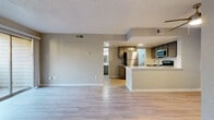This single-floor residence is designed with an open-concept layout that seamlessly connects the living area to the kitchen, creating a cohesive and functional living space. Light-toned, wood-look flooring runs throughout, complementing the neutral gray walls and white baseboards to establish a clean, modern aesthetic. The textured ceilings add a subtle architectural detail consistent across the unit.

The kitchen is well-appointed with gray cabinetry, a white countertop peninsula, and a full suite of stainless steel appliances including a refrigerator, electric range, over-the-range microwave, and dishwasher. A white subway tile backsplash adds a contemporary touch, while a ceiling fan overhead provides additional ventilation. The peninsula offers a natural divide between the kitchen and living areas.

The living space is generously proportioned, with a sliding glass door providing direct access to a private outdoor area and allowing natural light to filter in. A dedicated bedroom includes a walk-in closet with built-in shelving, offering ample storage. Additional utility space houses a water heater with nearby shelving. The entry door opens into a welcoming foyer area that transitions smoothly into the main living space.