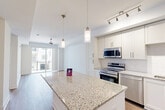 Located at 9113 Baltimore Ave in College Park, MD, this single-floor residence offers a thoughtfully designed open-concept layout that seamlessly integrates the living, dining, and kitchen areas. The kitchen is a standout feature, showcasing crisp white shaker cabinetry reaching to the ceiling, granite countertops, a large central island with pendant lighting, and a full suite of stainless steel appliances including a range, microwave, dishwasher, and refrigerator. Track lighting and a subway tile backsplash complete the polished look. The living area features warm wood-tone flooring, a ceiling fan, and large sliding glass doors that open to a private balcony, filling the space with natural light. The bedroom is finished with plush carpet, a ceiling fan, and direct access to both a spacious walk-in closet with multi-tier wire shelving and the full bathroom. The bathroom is elegantly appointed with a dual-sink granite vanity, a large mirror, tile flooring, and a tiled soaking tub. Additional conveniences include a dedicated laundry area and a utility room, rounding out this efficiently designed and modern residence.