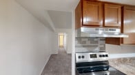 This single-floor residence offers three bedrooms, one bathroom, and a thoughtfully arranged layout that maximizes functionality. The galley-style kitchen is a standout feature, outfitted with warm honey-toned wood cabinetry, stone-patterned laminate countertops, a double stainless steel sink, a stainless steel refrigerator, a dishwasher, and an electric range with a tile backsplash and under-cabinet range hood. Recessed lighting and a pendant chandelier illuminate the space, while light tile flooring adds a clean, classic finish. The open living area extends from the kitchen, featuring neutral carpet, white walls, and a sliding glass door that invites natural light. A central hallway connects the bedrooms and bathroom, all finished with plush carpeting. The primary bedroom offers a roomy closet with bifold doors and built-in rod and shelf storage. Additional bedrooms are bright and comfortable, with one featuring a window with an outdoor view. The bathroom includes a white vanity with a single basin sink, a medicine cabinet mirror, and wood-look flooring. Throughout the residence, a consistent neutral palette and clean architectural lines create a calm, functional living environment.