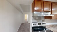 This single-floor residence offers three bedrooms, one bathroom, and a thoughtfully arranged layout that maximizes functionality. The galley-style kitchen is a standout feature, outfitted with warm honey-toned wood cabinetry, stone-patterned laminate countertops, a double stainless steel sink, a stainless steel refrigerator, a dishwasher, and an electric range with a tile backsplash and under-cabinet range hood. Recessed lighting and a pendant chandelier illuminate the space, while light tile flooring adds a clean, classic finish. The open living area extends from the kitchen, featuring neutral carpet, white walls, and a sliding glass door that invites natural light. A central hallway connects the bedrooms and bathroom, all finished with plush carpeting. The primary bedroom offers a roomy closet with bifold doors and built-in rod and shelf storage. Additional bedrooms are bright and comfortable, with one featuring a window with an outdoor view. The bathroom includes a white vanity with a single basin sink, a medicine cabinet mirror, and wood-look flooring. Throughout the residence, a consistent neutral palette and clean architectural lines create a calm, functional living environment.