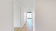 This contemporary 2-bedroom, 2-bathroom residence offers a well-designed single-level layout with a clean, modern aesthetic throughout. The living room is a standout space, anchored by expansive floor-to-ceiling windows that frame sweeping panoramic city views and flood the interior with abundant natural light. Exposed concrete ceilings add an industrial character that contrasts beautifully with crisp white walls and light-toned hardwood flooring found throughout the unit. Track lighting in the living areas provides both functionality and a refined urban edge.

The kitchen is outfitted with two-tone cabinetry — light wood uppers paired with white lower cabinets — complemented by quartz countertops, a stainless steel refrigerator, and matte black fixtures including a sleek gooseneck faucet. The primary bedroom is a spacious retreat with its own city views through large windows, while the second bedroom offers a similarly clean, open feel with concrete ceiling details. Both rooms share access to well-appointed bathrooms. The primary bath features a floating double-vanity with wood cabinetry, dual mirrors with integrated lighting, and a glass-enclosed walk-in shower. The secondary bathroom includes a tub-shower combination with white subway tile and matte black hardware. Three hallways, a closet, and thoughtful circulation complete this refined urban residence.