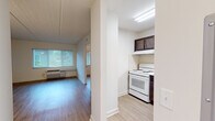 Located at 9050 Norfolk Blvd in Jacksonville, FL, this single-floor unit offers a clean, functional layout with consistent wood-look flooring throughout. The living area is bright and open, featuring a large window fitted with horizontal blinds that invite natural light and offer views of the surrounding greenery. A wall-mounted HVAC unit ensures year-round climate comfort, and a textured ceiling adds a classic finishing touch.

The kitchen is well-appointed with rich dark wood cabinetry, brushed nickel hardware, and crisp white countertops that provide ample prep space. An L-shaped layout maximizes storage and workspace, complemented by a stainless steel sink and a white electric range with overhead cabinetry.

The bedroom is a comfortable, well-lit space with its own window overlooking the outdoors and a ceiling fan for added ventilation. Light-toned wood-look flooring continues seamlessly into this room, maintaining a cohesive aesthetic throughout the unit.

The bathroom is thoughtfully designed with accessibility in mind, featuring stainless steel grab bars around the tub and shower area, white subway tile surround, a clean vanity with a dark wood base, and light flooring. The overall design of the space is neutral and move-in ready, offering a practical and welcoming environment.