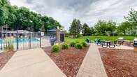Located at 5707 MN-7 E in St. Louis Park, Minnesota, this multi-story residential building combines classic brick and siding construction with a well-maintained exterior designed for both function and comfort. The building's façade features a welcoming central entrance framed by a navy awning, flanked by decorative lamp posts and neatly landscaped mulched beds that lead residents and visitors along a clean concrete pathway to the front doors. Each floor is lined with private balconies outfitted with white railings, offering residents their own outdoor retreat with views of the surrounding greenery. The outdoor common areas are a standout feature of this property. A fenced swimming pool with lounge seating and shaded umbrella tables provides a resort-like setting for relaxation and recreation. Adjacent to the pool, a brick-paved patio with Adirondack chairs and picnic seating creates a casual gathering space. A generous open lawn area, framed by mature trees, adds to the park-like atmosphere, while a built-in grill station makes outdoor cooking convenient. The grounds are thoughtfully landscaped throughout with flowering plants, mulched garden beds, and lush grass, offering a serene environment. The property's setting along MN-7 provides convenient access to the broader St. Louis Park community.