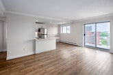Unit 803 at 38 King St W in Hamilton presents a well-designed two-bedroom, one-bathroom residence spread across a single floor. Light wood-tone laminate flooring runs throughout, creating a cohesive and clean aesthetic from room to room.

The open-concept kitchen and living area forms the heart of the unit. The kitchen features white shaker-style cabinetry with brushed gold hardware, stainless steel appliances including a refrigerator, stove, and built-in microwave, and a light-toned countertop with an integrated sink. A tall pantry cabinet provides additional storage. Recessed lighting illuminates the galley-style workspace, which flows naturally into the living area. The living room benefits from a sliding glass door that opens to a private balcony, filling the space with natural light. A wall-mounted ductless air conditioning unit and baseboard heaters provide year-round climate control.

Both bedrooms are finished with the same warm flooring and neutral walls. The primary bedroom includes a wall-mounted AC unit and a window with an outdoor view. The second bedroom features a double-door closet. The bathroom is fitted with a soaking tub and subway tile surround. In-unit laundry adds further convenience to this efficiently arranged home.