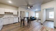 Located at Graystone Landing on East Berry Street in Fort Wayne, Indiana, this single-floor unit offers a clean, modern design with consistent wood-look flooring running throughout every room. The open-concept layout connects the kitchen and living area into one cohesive space, creating a functional and comfortable environment.

The kitchen is equipped with white cabinetry, a full-size refrigerator, electric range with overhead microwave, dishwasher, and a sink with light countertops. A high-top dining table fits naturally within the kitchen footprint, making efficient use of the shared space. A ceiling fan with integrated lighting is mounted overhead, providing both airflow and illumination across the open area.

The living room receives natural light through a window and features a wall-mounted TV bracket with pre-installed wiring for a streamlined setup. The space is open enough to accommodate varied furniture arrangements.

The bedroom is a well-proportioned, private room with its own window and ceiling fan. A connecting hallway provides access to additional storage or closet space.

The bathroom features a white vanity, toilet, and a shower with a curtain rod, all finished with the same wood-look flooring found throughout the unit. Neutral wall tones across all rooms contribute to a cohesive, move-in-ready atmosphere.