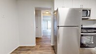 This two-story home offers a practical and clean layout across two levels, combining updated finishes with functional living spaces throughout. The main level features hardwood-style flooring that flows seamlessly from the kitchen through the hallway and into the living area. The kitchen is equipped with stainless steel appliances — including a refrigerator, oven, microwave, and dishwasher — complemented by white shaker-style cabinetry and dark countertops that provide a sharp contrast. The living room is a standout space, highlighted by a white stone fireplace and a sliding glass door fitted with vertical blinds that opens to an outdoor patio, allowing for generous natural light. A carpeted staircase with an ornate white wrought-iron railing connects the main level to the upper floor. The upper level hosts multiple bedrooms, each finished with neutral carpet, vertical blind-covered windows, and ample built-in closet storage. A full bathroom with a tub-shower combination and hardwood-style flooring serves the upper level. Textured ceilings are consistent throughout the home, adding a classic architectural touch. The overall aesthetic is bright, clean, and move-in ready.