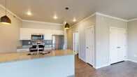 Located at 2760 47th St S in Fargo, North Dakota, this well-appointed single-floor residence offers a thoughtfully designed open-concept layout that seamlessly connects the kitchen, dining, and living areas. The kitchen is a standout feature, boasting granite countertops, crisp white cabinetry, a subway tile backsplash, and a full suite of stainless steel appliances including a refrigerator, electric range, and over-the-range microwave. Stylish pendant lighting and recessed fixtures illuminate the space, while a central island with a double sink adds both function and visual appeal. Crown molding throughout lends a polished, finished look to every room. The open living area is bathed in natural light from a sliding glass door that leads to a private balcony, complemented by warm wood-look flooring that flows throughout the entire unit. The bedroom is generously proportioned, featuring a double-door closet and a window providing additional natural light. The bathroom includes a full tub-and-shower combo, granite vanity countertop, and dark wood cabinetry. A dedicated in-unit laundry area houses a stacked washer and dryer for added convenience. The neutral color palette and clean architectural lines create a modern, inviting ambiance throughout.