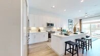 This thoughtfully designed 1-bedroom, 1-bathroom residence offers a functional and stylish layout across a single floor. The open-concept kitchen is a standout feature, showcasing floor-to-ceiling white shaker cabinetry, a herringbone tile backsplash, stainless steel appliances including a French door refrigerator and electric range, and a generous island with a waterfall-edge countertop and bar seating — ideal for casual dining or entertaining. Light hardwood flooring runs throughout the main living areas, enhancing the bright, airy atmosphere. The living room is bathed in natural light from large sliding glass doors that open to a private balcony with open outdoor views, creating a seamless indoor-outdoor connection. The bedroom offers plush carpeting, a well-sized window with natural light, and a dedicated closet for ample storage. The full bathroom features light hardwood flooring, a sleek white vanity with under-cabinet storage, a large mirror, and a glass-enclosed walk-in shower. Recessed lighting and a clean, neutral color palette tie the entire space together, creating a modern and welcoming ambiance throughout.