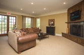 This single-floor space offers a thoughtfully designed layout with warm, traditional finishes throughout. The main living area serves as the centerpiece, anchored by a striking corner fireplace framed by rich, dark wood built-in cabinetry and a granite surround. Neutral carpet and warm golden-toned walls create a welcoming ambiance, complemented by crown molding that adds an elegant architectural touch.

Adjacent to the living area is a built-in bar with dark wood high-back barstools, ideal for entertaining. The space flows seamlessly into a separate sitting room, where light tile flooring, white trim, and a pair of classic accent chairs create a calm and refined retreat.

A bright dining nook bathed in natural light features large gridded windows overlooking a balcony and outdoor greenery, lending an airy, relaxed feel. Woven rattan chairs surround a round glass-top table, reinforcing the space's classic yet comfortable character.

A generously sized lounge area includes elegant French doors with multi-pane glass panels that open to an outdoor balcony, filling the room with natural light. Soft carpeting, neutral tones, and tasteful décor complete this inviting area.

Throughout, the space maintains a cohesive aesthetic defined by warm earth tones, traditional millwork, and an abundance of natural light.