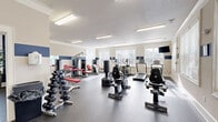 Located at 101 Halehaven Dr in Duncan, SC, this fitness center offers a thoughtfully designed exercise space spread across a single floor. The main workout area is bright and open, with large windows along the walls that invite natural light and provide views of the surrounding community. A bold navy and cream color scheme runs throughout, with a decorative horizontal stripe accenting the walls, giving the space a polished, cohesive look. Durable speckled rubber flooring covers the entire facility, providing both safety and comfort underfoot.

The main exercise floor is generously proportioned, housing a comprehensive array of equipment including multiple treadmills, elliptical trainers, stationary bikes, and a variety of strength machines with red upholstered seats. A heavy bag and additional functional fitness equipment round out the offerings. Overhead, flush-mounted fluorescent lighting ensures the space remains well-lit at all times.

A separate flex room, painted in deep navy blue with crisp white crown molding and trim, provides a dedicated area for stretching, yoga, or light training. This room features a stability ball rack, a shelving unit stocked with accessories such as kettlebells and resistance tools, tasteful wall art, and an interior plant, creating a calm, welcoming environment. A pass-through window connects this room visually to the main floor, maintaining an open and connected feel throughout the facility.