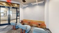 This 800 square foot recreational space is a testament to modern design and functionality. The open-plan layout is divided into distinct zones, each catering to different leisure activities. A striking feature is the mezzanine level, accessible via a sleek metal staircase, which overlooks the main area and adds vertical interest to the space.

The main floor boasts a variety of entertainment options. A full-sized foosball table takes center stage, accompanied by retro arcade machines that add a nostalgic touch. The "Discover" area features a pool table set against a teal accent wall with grid detailing, creating a focal point in the room.

Comfortable seating is strategically placed throughout, including modern grey sofas and uniquely designed blue chairs, perfect for relaxation or casual conversations. The space also incorporates a kitchenette area with wooden cabinetry and bar seating, ideal for preparing and enjoying refreshments.

Lighting is a key design element, with recessed ceiling lights, pendant lamps, and a striking geometric light fixture that adds drama and illumination. Large windows allow natural light to flood the space, while also offering views of the surrounding area.

The flooring is a mix of polished concrete and patterned tiles, adding texture and visual interest. White brick walls provide a neutral backdrop that enhances the overall contemporary aesthetic. This versatile space successfully combines style and functionality, creating an inviting environment for various recreational activities.