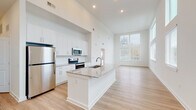 Located at 680 Hamilton Ave SE in Atlanta's Grant Park area, this single-floor residence showcases a clean, modern design throughout. The open-concept living and kitchen area is anchored by soaring ceilings and an abundance of natural light streaming through oversized windows, creating a bright and airy atmosphere. Light wood-tone flooring runs throughout the main living spaces, complementing the crisp white walls and recessed lighting above.

The kitchen is a standout feature, equipped with white shaker-style cabinetry, granite countertops, stainless steel appliances including a refrigerator, electric range, and microwave, and a centrally positioned island with a built-in sink — ideal for both cooking and casual entertaining. The open layout allows the kitchen to flow seamlessly into the expansive living area.

The bedroom is carpeted for comfort and benefits from tall ceilings and a large window, with direct access to a private balcony offering neighborhood views. An en-suite bathroom features a granite-topped vanity with white cabinetry, while a spacious walk-in closet with built-in shelving provides generous storage. The unit's contemporary finishes and thoughtful layout make it a refined and functional living space.