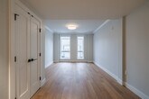 Located at 314 N Cayuga St in Ithaca, NY, this well-designed one-bedroom, one-bathroom unit offers a thoughtful layout across a single floor. The living room is bathed in natural light from a pair of large double-hung windows that frame views of the surrounding neighborhood, including a charming stone building across the street. Light hardwood flooring flows throughout the main living areas, enhancing the bright, clean aesthetic defined by crisp white trim and neutral gray walls.

The kitchen is a standout feature, boasting a galley-style configuration with gray shaker cabinetry, white quartz countertops, a subway tile backsplash, recessed lighting, and a full suite of stainless steel appliances including a range with hood and a French door refrigerator. Hardwood flooring continues here, tying the space together seamlessly.

The bedroom is a comfortable, carpeted retreat featuring a tall window that brings in natural light and a view of the street. A hallway connects the bedroom to additional closet space and the full bathroom, which is finished with large-format tile flooring, a vanity with sink, and accessibility-friendly grab bars throughout.

The overall ambiance is modern and clean, with a neutral palette and quality finishes that make this Ithaca unit a polished and functional living space.