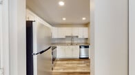 This single-floor unit offers a clean, contemporary design with a neutral color palette and wood-look flooring that flows consistently throughout every room. The kitchen serves as a functional centerpiece, featuring white shaker-style cabinetry with brushed nickel hardware, neutral countertops, and a full suite of stainless steel appliances including a refrigerator, electric range, over-the-range microwave, and dishwasher. A deep double-basin sink with a flexible pull-down faucet completes the well-organized layout, which is illuminated by recessed ceiling lighting.

The unit includes multiple bedrooms, each finished with the same wood-look flooring and neutral wall tones. Bedrooms are equipped with closets, and at least one room features a window with vertical blinds that allows natural light to enter. The open living area benefits from recessed lighting and direct access to natural light through large windows.

Two bathrooms serve the unit. The full bathroom includes a soaking tub, a vanity with white cabinetry and a single sink, and a large mirror. A second bathroom features a glass-enclosed shower stall. Both bathrooms are finished with wood-look flooring and chrome fixtures, maintaining a cohesive aesthetic throughout the space.