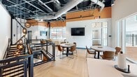 Located at 2940 Falstaff Rd in Raleigh, NC, this contemporary multi-level commercial space blends industrial-chic aesthetics with modern comfort across three distinct floors. The design is immediately striking, with exposed black steel ceiling beams, open ductwork, and soaring ceiling heights that create a bold, warehouse-inspired atmosphere throughout.

The main level — the largest of the three floors — serves as a dynamic gathering and lounge area. It features eye-catching herringbone light wood flooring, warm accent walls in terracotta orange, and abundant natural light from large windows overlooking the surrounding greenery and parking areas. Flexible seating arrangements include round tables with leather chairs and a mounted flat-screen display, making the space well-suited for collaboration or casual meetings. A sculptural pendant chandelier with circular metallic rings adds an artistic focal point near the mezzanine-style open railing.

Black metal railings with wire mesh paneling connect the levels, adding an industrial elegance that ties the design together. The lower levels provide additional functional areas, including a well-appointed kitchenette with light wood cabinetry, white quartz countertops, a bold hexagonal mosaic tile backsplash in teal and navy, a built-in microwave, and a stainless steel refrigerator. Tall windows in the kitchenette flood the space with natural light and offer outdoor views, enhancing the overall sense of openness.
