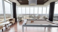 This elegant amenity lounge is designed to impress, combining recreational and social spaces within a single, open-concept floor. Floor-to-ceiling glass windows wrap the perimeter, flooding the room with natural light and offering expansive panoramic views of the surrounding cityscape, greenery, and waterway beyond — a defining feature of the space. Rich hardwood flooring grounds the interior and complements the contemporary aesthetic throughout.

At the heart of the lounge sits a sleek, modern billiards table in neutral tones, perfect for leisure and social gatherings. Surrounding it, curated seating arrangements — including plush armchairs and stylish round tables — provide comfortable spots for conversation and relaxation. A striking cylindrical column adds an architectural accent, while a bold drum pendant light anchors the ceiling above.

The ceiling itself is a design highlight, featuring a grid of dark wood slat panels that introduce warmth and texture, contrasting beautifully with the brightness of the glass walls. The overall ambiance is refined yet inviting — a polished space that balances contemporary design with a sense of openness and connection to the outdoors.