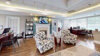 Located at 50 Pleasant Run Dr in Henrico, Virginia, this single-story professional office space combines a warm, inviting aesthetic with functional design. The interior is anchored by a sophisticated main area featuring a classic white fireplace with a mounted flat-screen display above it, tray ceilings with ambient lighting, and rich hardwood flooring throughout. Elegantly patterned accent chairs and comfortable seating arrangements create a welcoming atmosphere for clients and staff alike.

The reception and waiting area is bathed in natural light, thanks to expansive floor-to-ceiling windows fitted with horizontal blinds that offer views of the lush, tree-lined surroundings. A teal and gray color palette lends a calm, professional tone to the space. One windowed lounge area features a neutral sofa, a modern coffee table, and a coordinating area rug, creating a relaxed yet polished environment.

A dedicated workspace area accommodates multiple workstations with substantial desks, ideal for a collaborative office setting. An additional windowed room provides a bright, focused workspace with built-in desk surfaces and serene outdoor views. Throughout the space, hardwood floors, recessed lighting, drop ceilings, and thoughtful furnishings combine to deliver a professional yet comfortable office environment suited for client-facing business operations.