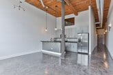 Located at 710 Greenville St in LaGrange, Georgia, this single-floor space showcases a compelling blend of industrial character and contemporary renovation. The design aesthetic is defined by soaring ceilings clad in warm wood planking, exposed ductwork, and polished concrete floors that carry a rich, reflective patina throughout the unit, creating a cohesive and visually striking environment.

The kitchen is a standout feature, boasting gray shaker-style cabinetry, dark stone countertops, stainless steel appliances including a range and microwave, and a decorative patterned tile backsplash. A peninsula with bar seating opens to the adjacent living area, which is bathed in natural light from oversized industrial-grid windows offering views of the surrounding landscape. Pendant lighting with globe fixtures adds warmth to the soaring ceiling above.

A hallway connects the living spaces to the private areas of the unit, which include a spacious bedroom with a walk-in closet fitted with built-in shelving. Two bathrooms provide well-appointed finishes, including dark stone vanity tops, shaker-style cabinetry, round mirrors, and brushed nickel hardware. One bathroom features a tiled tub-shower combination with vertical subway tile, while the other includes a vessel sink and full vanity setup. The overall ambiance is modern, clean, and loft-inspired.