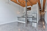 Located at 710 Greenville St in LaGrange, Georgia, this single-floor space showcases a compelling blend of industrial character and contemporary renovation. The design aesthetic is defined by soaring ceilings clad in warm wood planking, exposed ductwork, and polished concrete floors that carry a rich, reflective patina throughout the unit, creating a cohesive and visually striking environment.

The kitchen is a standout feature, boasting gray shaker-style cabinetry, dark stone countertops, stainless steel appliances including a range and microwave, and a decorative patterned tile backsplash. A peninsula with bar seating opens to the adjacent living area, which is bathed in natural light from oversized industrial-grid windows offering views of the surrounding landscape. Pendant lighting with globe fixtures adds warmth to the soaring ceiling above.

A hallway connects the living spaces to the private areas of the unit, which include a spacious bedroom with a walk-in closet fitted with built-in shelving. Two bathrooms provide well-appointed finishes, including dark stone vanity tops, shaker-style cabinetry, round mirrors, and brushed nickel hardware. One bathroom features a tiled tub-shower combination with vertical subway tile, while the other includes a vessel sink and full vanity setup. The overall ambiance is modern, clean, and loft-inspired.