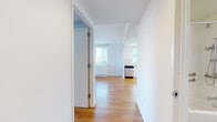 This well-appointed single-floor residence offers a clean, contemporary design defined by crisp white walls, warm honey-toned hardwood flooring, and an abundance of natural light. An entry hallway leads seamlessly into the open living area, where large windows frame urban views and fill the space with daylight.

The kitchen is thoughtfully designed with white cabinetry extending to the ceiling, a classic subway tile backsplash, and a full suite of stainless steel appliances including a range, microwave, dishwasher, and refrigerator. The layout is efficient yet generous, with ample counter and storage space.

The living area is open and airy, with clean sightlines and continuity in the hardwood flooring that enhances the sense of space. Multiple rooms benefit from windows with city views, and select rooms include access to outdoor areas, allowing for fresh air and additional natural light.

The bathroom is finished in neutral grey floor tiles and features a full soaking tub with shower, wall-mounted vanity with an integrated sink, a large mirror, and accessibility grab bars throughout, reflecting a thoughtful and inclusive design approach.

Overall, the residence presents a bright, modern aesthetic with consistent finishes and a functional layout suited to comfortable everyday living.