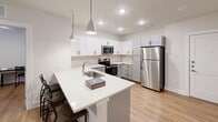 This single-floor, two-bedroom, two-bathroom unit in Austin, Texas offers a well-designed, modern living environment with a clean, contemporary aesthetic. The open-concept layout connects the kitchen, dining, and living areas into one cohesive space, creating an efficient and welcoming atmosphere.

The kitchen is a standout feature, equipped with stainless steel appliances including a refrigerator, electric range, and built-in microwave. White upper cabinetry contrasts with gray lower cabinets, complemented by a neutral tile backsplash and white quartz countertops. A peninsula with an undermount sink and pendant lighting above serves as both a workspace and casual dining area.

The living area features warm wood-look flooring, a ceiling fan, and a large window that allows ample natural light. Both bedrooms are comfortably sized with ceiling fans, windows fitted with blinds, and wood-look flooring throughout.

Each bathroom reflects the unit's modern design language, with white shaker-style cabinetry, quartz countertops, black hardware accents, and large-format gray tile surrounding the tub-shower combination. One bathroom also includes a walk-in closet accessible from the hallway. The overall aesthetic is clean, neutral, and well-appointed throughout.