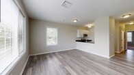This single-floor, one-bedroom, one-bathroom unit at 3 Schooner in Milford, CT offers a clean, modern interior with a neutral color palette throughout. The open living area is finished with light hardwood-style flooring and features a large window that brings in natural light, creating a bright and welcoming atmosphere. The space flows seamlessly into the kitchen, which is accessible via a half-wall pass-through. The kitchen is equipped with white cabinetry featuring sleek bar-pull hardware, dark granite countertops, and stainless steel appliances including an electric range and over-the-range microwave. The bedroom is comfortably sized, finished with plush carpeting, and includes a generous walk-in closet with built-in shelving for ample storage. A secondary room with a standard closet provides additional flexibility. The full bathroom is well-appointed with white cabinetry, dark granite countertops, a single undermount sink, and a tub-shower combination with a glass sliding door. Tile flooring completes the bathroom's polished look. The unit's consistent neutral tones, quality finishes, and practical layout combine to create a comfortable and functional living environment.