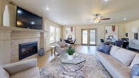 Located in Moore, Oklahoma, this single-floor space offers a thoughtfully designed layout that seamlessly integrates a living room, dining area, and kitchen into a cohesive and functional environment. The living room serves as the heart of the space, anchored by a tile-surround fireplace with a classic mantel and a wall-mounted television above. Multiple windows flood the room with natural light, while ceiling fans add comfort overhead. A set of French doors opens to the exterior, enhancing the sense of openness. Comfortable seating arrangements, a geometric glass coffee table, and tasteful artwork contribute to the welcoming ambiance throughout. The dining area features a round wood table with upholstered chairs and benefits from additional windows that frame outdoor views, complemented by decorative round mirrors on the wall. The kitchen is equipped with rich dark wood cabinetry, granite-style countertops, and black appliances, including a side-by-side refrigerator and electric range. A peninsula with bar seating provides a convenient casual dining option. Light tile flooring runs consistently throughout, tying the spaces together with a clean, neutral aesthetic that is both practical and inviting.