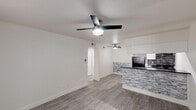 Located at 3802 N 27th St in Phoenix, Arizona, this single-floor unit offers a clean, modern aesthetic throughout. The open-concept living and dining area is finished with light wood-look flooring and features ceiling fans for comfort in the Arizona climate. A standout element is the kitchen's stone-clad breakfast bar, which defines the boundary between the living space and the galley-style kitchen. The kitchen itself is outfitted with white shaker cabinetry, dark granite-style countertops, black appliances including a range and refrigerator, a stainless steel sink, and track lighting overhead — offering both functionality and style in a compact, efficient layout. Natural light filters into the space through windows dressed with vertical blinds, contributing to a bright and airy atmosphere. The bedroom features plush carpeting, a ceiling fan, and a window that brings in additional natural light. The bathroom is finished with wood-look flooring and includes a full shower-tub combination with clean white surrounds and a dark-topped vanity. The entry area provides a welcoming transition into the home, with light flooring and a window that enhances the sense of openness. Overall, this unit presents a well-maintained, contemporary living environment suited for Phoenix's lifestyle.