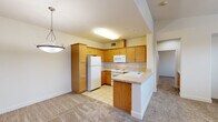 This two-story residence offers a thoughtful layout spread across two levels, with the garage and entry on the ground floor and the primary living spaces above. The attached garage features a concrete floor, automatic door opener, and direct interior access through a paneled door, providing convenient and secure entry.

A carpeted staircase with a white handrail leads up to the main living level, where an open-concept kitchen and living room create a bright, cohesive gathering space. The kitchen is equipped with warm honey-toned wood cabinetry, a full suite of white appliances including a refrigerator, range, and built-in microwave, and a peninsula with a sink that extends into the living area. Light tile flooring transitions seamlessly from the kitchen into the carpeted living room, which is illuminated by a ceiling fan and pendant lighting.

The spacious bedroom is bathed in natural light through multiple large windows dressed with horizontal blinds, offering views of the surrounding neighborhood. A ceiling fan overhead and plush wall-to-wall carpet add comfort throughout. A dedicated closet provides practical storage adjacent to the bedroom.

The full bathroom features tile flooring, a wood-toned vanity with a white countertop, a backlit mirror, and a tub-shower combination. Neutral, warm tones carry throughout the entire residence, lending a cohesive and inviting ambiance.