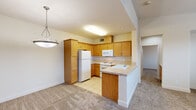 This two-story residence offers a thoughtful layout spread across two levels, with the garage and entry on the ground floor and the primary living spaces above. The attached garage features a concrete floor, automatic door opener, and direct interior access through a paneled door, providing convenient and secure entry.

A carpeted staircase with a white handrail leads up to the main living level, where an open-concept kitchen and living room create a bright, cohesive gathering space. The kitchen is equipped with warm honey-toned wood cabinetry, a full suite of white appliances including a refrigerator, range, and built-in microwave, and a peninsula with a sink that extends into the living area. Light tile flooring transitions seamlessly from the kitchen into the carpeted living room, which is illuminated by a ceiling fan and pendant lighting.

The spacious bedroom is bathed in natural light through multiple large windows dressed with horizontal blinds, offering views of the surrounding neighborhood. A ceiling fan overhead and plush wall-to-wall carpet add comfort throughout. A dedicated closet provides practical storage adjacent to the bedroom.

The full bathroom features tile flooring, a wood-toned vanity with a white countertop, a backlit mirror, and a tub-shower combination. Neutral, warm tones carry throughout the entire residence, lending a cohesive and inviting ambiance.