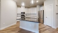This well-designed 2-bedroom, 2-bathroom residence in Leander, TX offers a thoughtful layout with modern finishes throughout. The kitchen is a standout feature, boasting white shaker cabinetry, dark granite countertops, a subway tile backsplash, stainless steel appliances including a gas range and French door refrigerator, and a central island with globe pendant lighting — ideal for cooking and entertaining. Light wood-style flooring flows through the main living areas, complementing the bright, neutral palette.

Both bathrooms are finished with white vanity cabinetry, dark granite countertops, and large mirrors. One bathroom includes a walk-in marble-tiled shower, while the second features a marble-surround soaking tub and shower combo. The generously sized primary bedroom includes plush carpet, direct access to its en-suite bathroom, and a spacious walk-in closet with built-in shelving and hanging rods. The second bedroom offers comfortable carpeted flooring and clean neutral walls.

A private balcony extends the living space outdoors, offering views of the landscaped community grounds, pool area, and open green space. The exterior presents a clean, contemporary aesthetic with crisp white finishes and modern architectural lines.