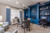 Located at Park Creek Court in Gainesville, Georgia, this single-floor professional office space combines sophisticated design with practical functionality. The interior is anchored by a striking built-in workstation finished in deep teal, featuring floor-to-ceiling open shelving, lower cabinetry, and dedicated computer and printer stations — providing an organized, fully equipped workspace for staff. Bold teal columns frame the built-ins and add a strong architectural focal point to the room.

A round glass-top meeting table surrounded by upholstered gray chairs with nailhead trim sits at the center, creating an inviting setting for consultations or collaborative discussions. Patterned navy and white curtains dress the large windows, allowing ample natural light to filter through while maintaining a cohesive, designed aesthetic.

A cozy lounge corner features a soft gray sofa and matching accent chair arranged around a glass side table, offering a relaxed seating area for visitors. Warm table lamps and framed artwork contribute to the welcoming ambiance throughout. Textured carpeting in a neutral tone grounds the space, complementing the warm gray walls. The overall design balances professional utility with an approachable, well-curated atmosphere suited for a leasing office or community clubhouse setting.